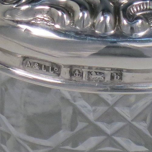 An Antique Victorian Sterling Silver and cut-crystal dressing table jar / box, having a round hand-cut crystal body in the Hobnail pattern, a hand-chased pull-off lid with floral decoration, and sitting on a flat star-cut base. Made by Adie & Lovekin Ltd., of Birmingham in 1901. The dimensions of this fine hand-made antique silver and crystal dressing table box / jar are height 8 cms (3 inches), and diameter 7 cms (2.75 inches).   