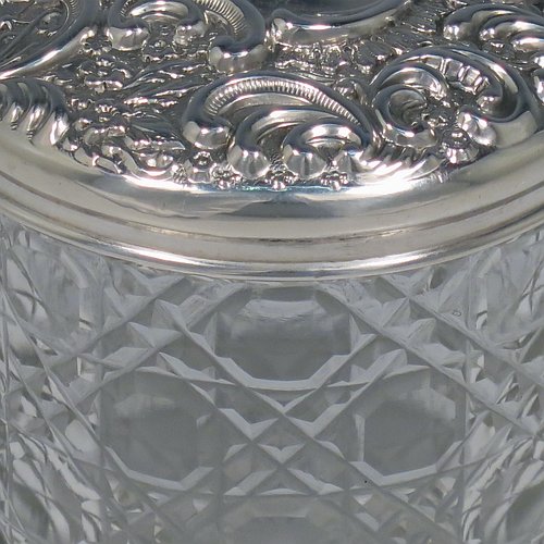 An Antique Victorian Sterling Silver and cut-crystal dressing table jar / box, having a round hand-cut crystal body in the Hobnail pattern, a hand-chased pull-off lid with floral decoration, and sitting on a flat star-cut base. Made by Adie & Lovekin Ltd., of Birmingham in 1901. The dimensions of this fine hand-made antique silver and crystal dressing table box / jar are height 8 cms (3 inches), and diameter 7 cms (2.75 inches).   