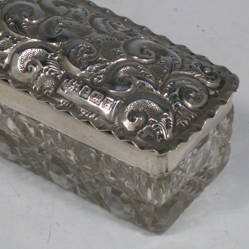 Antique Edwardian sterling silver and crystal dressing table jar / box, having a pull-off lid with hand-chased floral decoration, and a rectangular hand-cut crystal body. Made in Birmingham in 1909. Length 15 cms (6 inches), width 4 cms (1.5 inches), height 4 cms (1.5 inches).