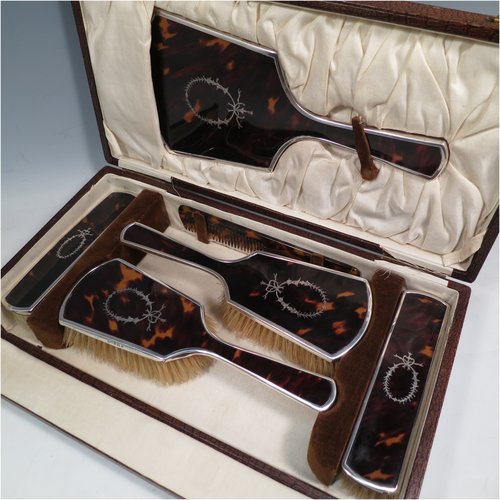 A Sterling Silver and inlaid tortoise-shell dressing table set with six pieces, consisting of a hand-mirror with original bevelled mirror, two clothes brushes, two hair brushes, all with original bristles, and a comb, all in original satin-lined presentation box. Made by Henry Matthews of Birmingham in 1924. The dimensions of this fine hand-made sterling silver and tortoiseshell dressing table service are length of mirror 27 cms (10.5 inches), and dimensions of box are length 37 cms (14.5 inches), width 19 cms (7.5 inches), and height 8.5 cms (3.3 inches). Please note that there is slight damage to the satin hinges.