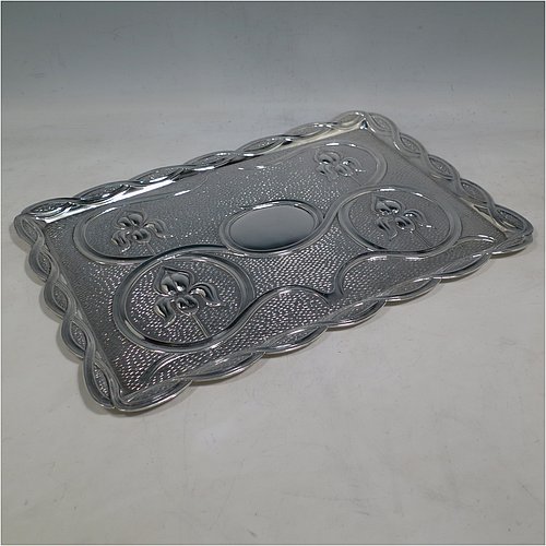 An Antique Edwardian Sterling Silver Arts and Crafts style dressing table pin tray, having a a shaped rectangular body with hand-chased scroll-work and lillies in a Rennie Mackintosh style, with a central vacant cartouche, and all sitting on a flat base. Made by A & J Zimmerman of Birmingham in 1902. The dimensions of this fine hand-made antique silver pin tray are length 33 cms (13 inches), width 22 cms (8.75 inches), and it weighs approx. 403g (13 troy ounces).    