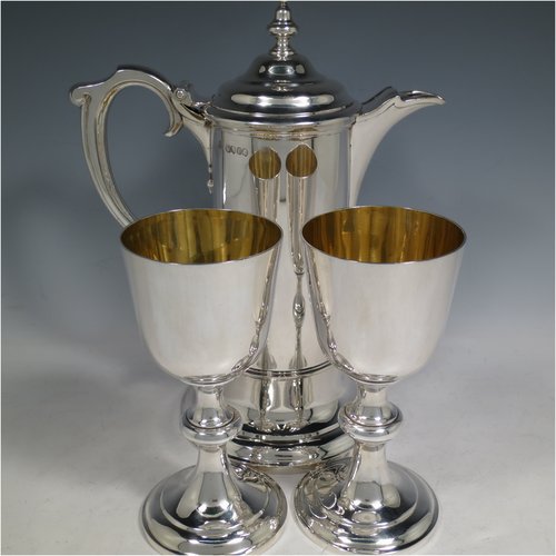 An Antique Victorian Sterling Silver communion service composed of a flagon and two goblets. The flagon in an early 17th century style having a straight-sided body, a scroll handle, a hinged & domed lid with urn-shaped finial, a matching scrolled spout and sitting on a collet foot. Together with a pair of plain round baluster goblets with gold-gilt interiors. All made by Robert Garrard of London in 1862/63. The dimensions of this fine hand-made communion set are height of flagon 29 cms (11.5 inches), length across handle & spout 23 cms (9 inches), height of goblets 18 cms (7 inches), and with a total weight of approx. 1,643g (53 troy ounces).   