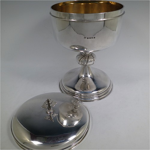 A very large and handsome Antique Edwardian Scottish Sterling Silver Ciborium, having a plain round body with a gold-gilt interior and applied reeded borders, sitting on a round pedestal foot with a swirl-fluted middle baluster, and a lift-off lid with double cruciform finial. Made by John Alexander Fettes of Glasgow in 1908. The dimensions of this fine hand-made and large antique silver ciborium and cover are height 28 cms (11 inches), diameter of cup 18.5 cms (7.25 inches), and it weighs a total of approx. 1,217g (39 troy ounces). Please note that this is the largest ciborium we have ever seen and is shown with a standard 75cl wine bottle for display purposes only and to give an indication of its size.