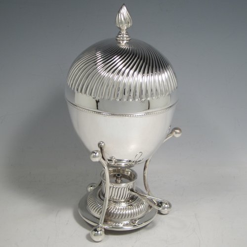 Antique Edwardian silver-plated egg coddler, having a plain round body, with lift-off lid having swirl fluting and a flame finial, and internal holder for four eggs, attached to a frame and stand with an original burner, all sitting on three ball feet. Made by Welbeck & Co., in ca. 1900. The dimensions of this fine hand-made silver plated egg coddler are height 23.5 cms (9.25 inches), and diameter 11 cms (4.3 inches).   