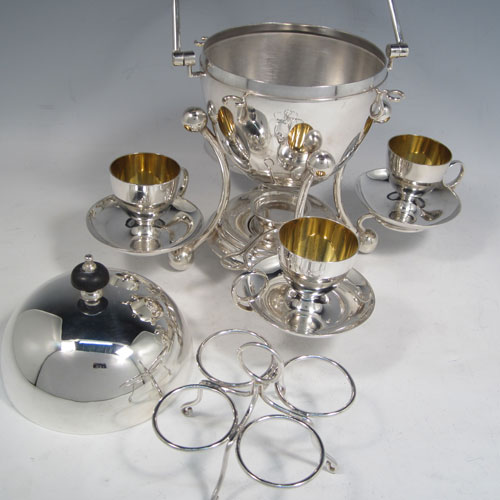 Antique Edwardian silver-plated egg coddler, having a plain round body with lift-off lid, sitting in a frame with swing handle, with four removable egg cups, an interior egg-holder, and an original burner, all sitting on four ball feet. Made in ca. 1900. The dimensions of this fine hand-made silver plated egg coddler are height 27 cms (10.5 inches), and width 26 cms (10.25 inches).