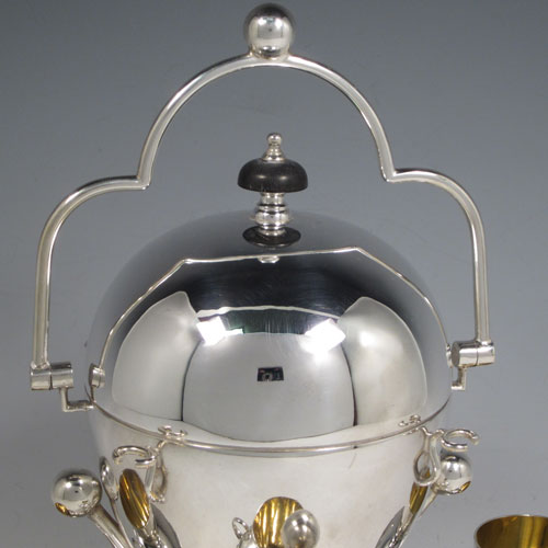 Antique Edwardian silver-plated egg coddler, having a plain round body with lift-off lid, sitting in a frame with swing handle, with four removable egg cups, an interior egg-holder, and an original burner, all sitting on four ball feet. Made in ca. 1900. The dimensions of this fine hand-made silver plated egg coddler are height 27 cms (10.5 inches), and width 26 cms (10.25 inches).