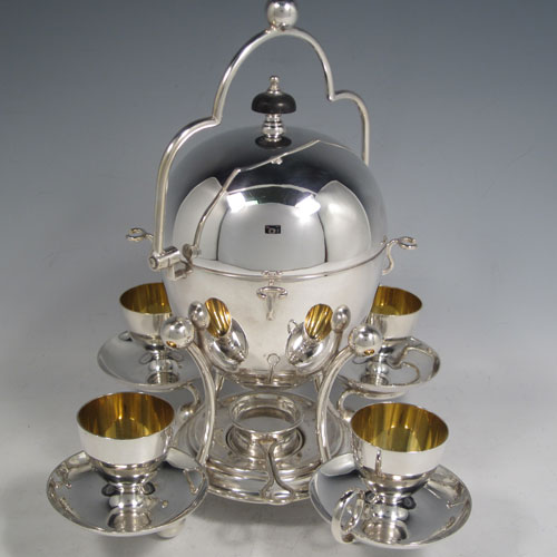 Antique Edwardian silver-plated egg coddler, having a plain round body with lift-off lid, sitting in a frame with swing handle, with four removable egg cups, an interior egg-holder, and an original burner, all sitting on four ball feet. Made in ca. 1900. The dimensions of this fine hand-made silver plated egg coddler are height 27 cms (10.5 inches), and width 26 cms (10.25 inches).