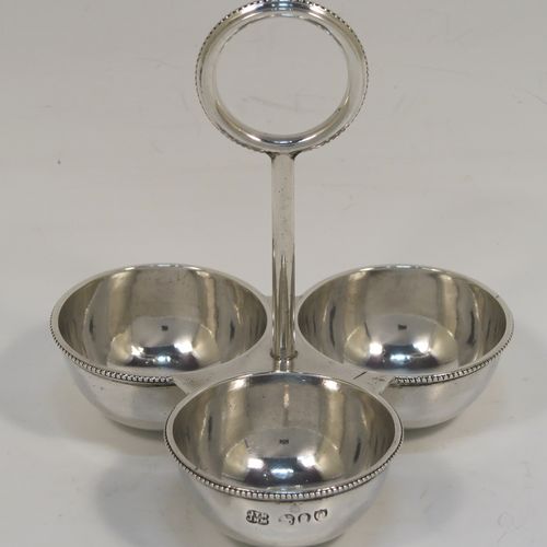 An elegant Antique Victorian Sterling Silver egg cruet or holder set, having three attached plain round bodied egg cups with applied bead-edged borders, and a ring handle above. This handsome antique egg holder was made by Heath and Middleton  of London in 1889. The dimensions of this fine hand-made silver egg holder are height 10 cms (4 inches), width 10 cms (4 inches), and it weighs approx. 82g (2.6 troy ounces).   