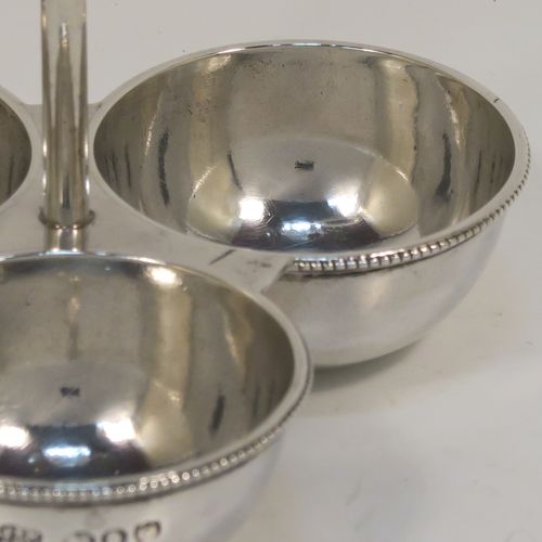 An elegant Antique Victorian Sterling Silver egg cruet or holder set, having three attached plain round bodied egg cups with applied bead-edged borders, and a ring handle above. This handsome antique egg holder was made by Heath and Middleton  of London in 1889. The dimensions of this fine hand-made silver egg holder are height 10 cms (4 inches), width 10 cms (4 inches), and it weighs approx. 82g (2.6 troy ounces).   