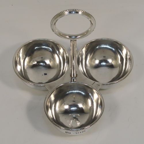 An elegant Antique Victorian Sterling Silver egg cruet or holder set, having three attached plain round bodied egg cups with applied bead-edged borders, and a ring handle above. This handsome antique egg holder was made by Heath and Middleton  of London in 1889. The dimensions of this fine hand-made silver egg holder are height 10 cms (4 inches), width 10 cms (4 inches), and it weighs approx. 82g (2.6 troy ounces).   