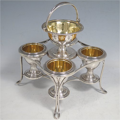 An Antique Georgian Sterling Silver egg cruet set, having four removable plain round egg cups, an unusual central condiment bowl for either salt or pepper with swing-handle, all with gold-gilt interiors, and all sitting in a wire-work frame stand with four feet. Made by Waterhouse, Hodson & Co., of Sheffield in 1828. The dimensions of this fine hand-made antique silver egg cruet set are height 18 cms (7 inches), width 17 cms (6.75 inches), with a total weight of approx. 530g (17 troy ounces).    