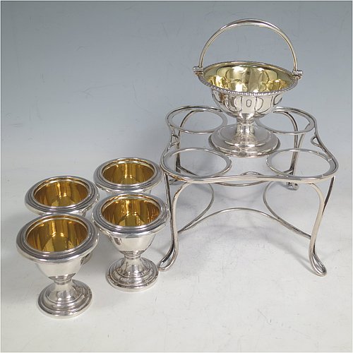 An Antique Georgian Sterling Silver egg cruet set, having four removable plain round egg cups, an unusual central condiment bowl for either salt or pepper with swing-handle, all with gold-gilt interiors, and all sitting in a wire-work frame stand with four feet. Made by Waterhouse, Hodson & Co., of Sheffield in 1828. The dimensions of this fine hand-made antique silver egg cruet set are height 18 cms (7 inches), width 17 cms (6.75 inches), with a total weight of approx. 530g (17 troy ounces).    