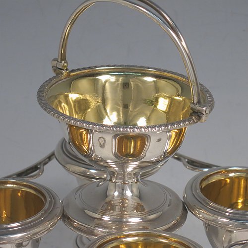 An Antique Georgian Sterling Silver egg cruet set, having four removable plain round egg cups, an unusual central condiment bowl for either salt or pepper with swing-handle, all with gold-gilt interiors, and all sitting in a wire-work frame stand with four feet. Made by Waterhouse, Hodson & Co., of Sheffield in 1828. The dimensions of this fine hand-made antique silver egg cruet set are height 18 cms (7 inches), width 17 cms (6.75 inches), with a total weight of approx. 530g (17 troy ounces).    