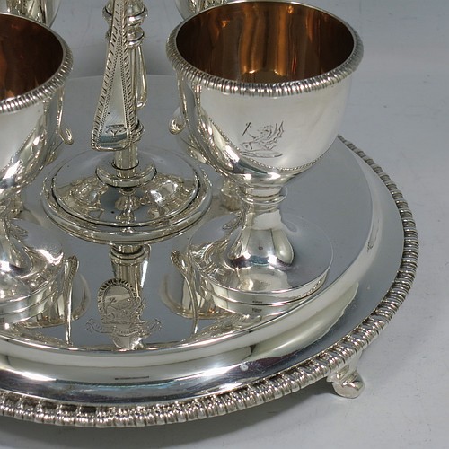 A very pretty Antique Victorian Sterling Silver egg cruet set, having a round body with applied gadroon borders, four plain round egg cups sitting on pedestal feet, and a cast loop handle attached to a round base sitting on four flange feet. Made by Andrew Crespel and Thomas Parker of London in 1867. The matching spoons are made by Jackson & Fullerton of London in 1906. The spoon and egg cup bowl interiors are all gold-gilt. The dimensions of this fine hand-made antique silver egg cruet set are height 18 cms (7 inches), diameter of base 17 cms (6.75 inches), and the total weight is approx. 856g (27.6 troy ounces). Please note that all items in this set are crested.