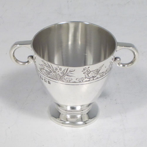 Sterling silver egg cup, having a plain round body with tapering sides, with a hand-engraved top border (showing ducks, ducklings, reeds, chickens, and chicks), with two scroll side-handles, and sitting on a pedestal foot. Made by R.W. Brookes for Harrods, London, in 1925. The dimensions of this fine hand-made silver egg cup are height 4.5 cms (1.75 inches), width 7 cms (2.75 inches), and it weighs approx. 44g (1.4 troy ounces).