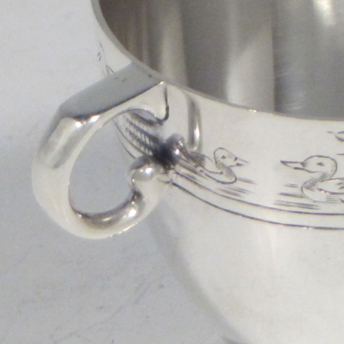 Sterling silver egg cup, having a plain round body with tapering sides, with a hand-engraved top border (showing ducks, ducklings, reeds, chickens, and chicks), with two scroll side-handles, and sitting on a pedestal foot. Made by R.W. Brookes for Harrods, London, in 1925. The dimensions of this fine hand-made silver egg cup are height 4.5 cms (1.75 inches), width 7 cms (2.75 inches), and it weighs approx. 44g (1.4 troy ounces).