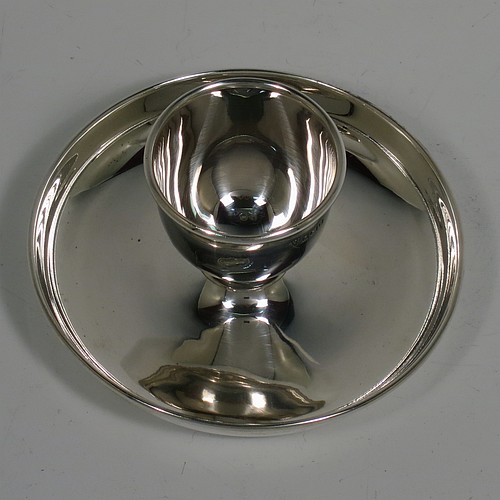 A Sterling Silver egg cup, having a plain round body with tapering sides, with an attached plain round plate with curved border, and sitting on a flat base. Made J. B. Chatterly of Birmingham in 1964. The dimensions of this fine hand-made silver egg cup are height 5 cms (2 inches), diameter 10 cms (4 inches), and it weighs approx. 87g (2.8 troy ounces).   