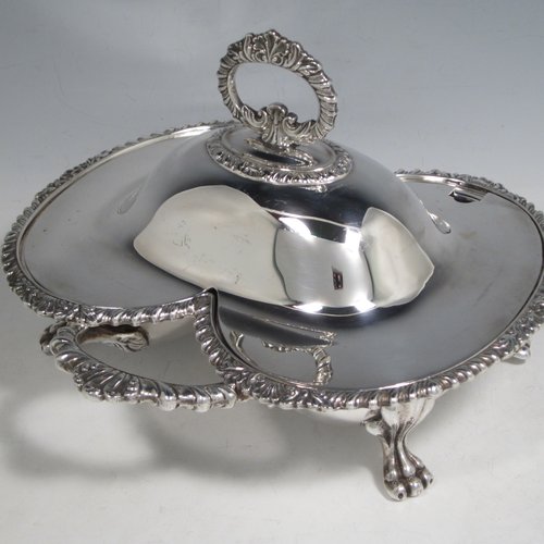 Antique Victorian silver plated double entree dish, having a very unusual double oval dish style, with removable cover and handle, applied gadroon and shell borders, a further side handle, and sitting on four cast lions-paw feet. Made in ca. 1890. The dimensions of this fine double entree dish and cover are height 15 cms (6 inches), length 23 cms (9 inches), and width 21.5 cms (8.5 inches).