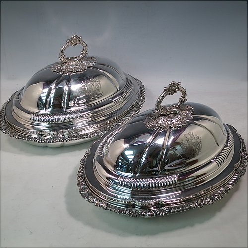 An Antique Georgian pair of Old Sheffield Plated entrée dishes with covers, having shaped oval bodies with with cast shell and gadroon borders, domed lids with hand-chased fluted decoration, and removable cast oak-leaf handles, and all sitting on flat bases. Made in ca. 1820. The dimensions of this pair of fine hand-made antique Georgian Old Sheffield Plated entrée dishes and covers are length 36 cms (14 inches), height including handle 21.5 cms (8.5 inches), and width 27.5 cms (10.75 inches). Please note that these are engraved with full armorial crests.   