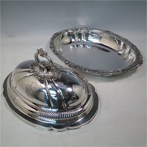 An Antique Georgian pair of Old Sheffield Plated entrée dishes with covers, having shaped oval bodies with with cast shell and gadroon borders, domed lids with hand-chased fluted decoration, and removable cast oak-leaf handles, and all sitting on flat bases. Made in ca. 1820. The dimensions of this pair of fine hand-made antique Georgian Old Sheffield Plated entrée dishes and covers are length 36 cms (14 inches), height including handle 21.5 cms (8.5 inches), and width 27.5 cms (10.75 inches). Please note that these are engraved with full armorial crests.   