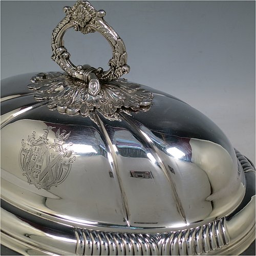 An Antique Georgian pair of Old Sheffield Plated entrée dishes with covers, having shaped oval bodies with with cast shell and gadroon borders, domed lids with hand-chased fluted decoration, and removable cast oak-leaf handles, and all sitting on flat bases. Made in ca. 1820. The dimensions of this pair of fine hand-made antique Georgian Old Sheffield Plated entrée dishes and covers are length 36 cms (14 inches), height including handle 21.5 cms (8.5 inches), and width 27.5 cms (10.75 inches). Please note that these are engraved with full armorial crests.   