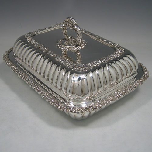 Antique Georgian Old Sheffield plated pair of entrée dishes with covers, having rectangular bodies and rounded corners, with hand-chased half-fluted decoration, applied cast floral bodies, and with removable bayonet-fit handles. All in original condition and made in ca. 1830. The dimensions of this fine pair of hand-made Old Sheffield plated entrée dishes and covers are length 28 cms (11 inches), width 23 cms (9 inches).