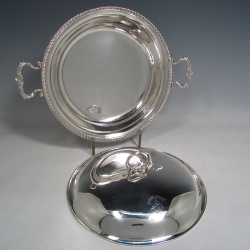 Antique Georgian sterling silver pair of entree or hash dishes with covers, having round bodies with applied gadroon borders and cast scroll side-handles, with plain domed lift-off covers having cast asparagus handles, an all sitting on flat bases. Made by Charles Wright of London in 1771. The dimensions of this pair of fine hand-made antique silver entree dishes and covers are diameter 24 cms (9.5 inches), height including cover handle 10 cms (4 inches), and they weigh a total of approx. 1,738g (56 troy ounces). Please note that both the bases and covers are crested.