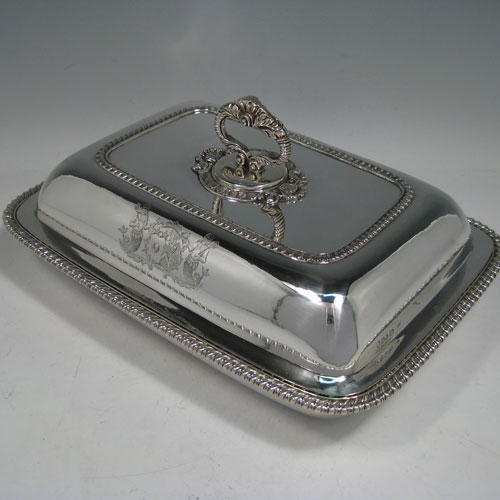 Antique Georgian pair of entree dishes with covers, having rectangular bodies with rounded corners, bayonet-fit removable gadroon and shell handles, gadroon borders, and sitting on flat bases. Made by Joseph Angell of London in 1817. The dimensions of this pair of fine hand-made antique silver entree dishes and covers are length 29 cms (11.5 inches), height including handle 13 cms (5 inches), width 21.5 cms (8.5 inches), and they weigh a total of approx. 3,120g (101 troy ounces). Please note that these are crested, and the Latin motto has been translated as The Moon Shall Fill Her Horns Again.