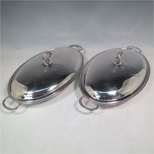 An Antique Georgian Sterling Silver pair of entree or hash dishes with covers, having oval bodies with applied bead-edged borders and cast loop side-handles, with plain domed lift-off covers having removable cast bead handles, and all sitting on flat bases. Made by Henry Green of London in 1790. The dimensions of this pair of fine hand-made antique silver entree dishes and covers are length 38 cms (15 inches), width 21.5 cms (8.5 inches), height including cover handle 11 cms (4.3 inches), and they weigh a total of approx. 2,077g (67 troy ounces). Please note that both the bases and covers are crested.   