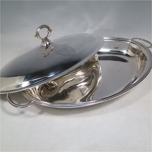 An Antique Georgian Sterling Silver pair of entree or hash dishes with covers, having oval bodies with applied bead-edged borders and cast loop side-handles, with plain domed lift-off covers having removable cast bead handles, and all sitting on flat bases. Made by Henry Green of London in 1790. The dimensions of this pair of fine hand-made antique silver entree dishes and covers are length 38 cms (15 inches), width 21.5 cms (8.5 inches), height including cover handle 11 cms (4.3 inches), and they weigh a total of approx. 2,077g (67 troy ounces). Please note that both the bases and covers are crested.   