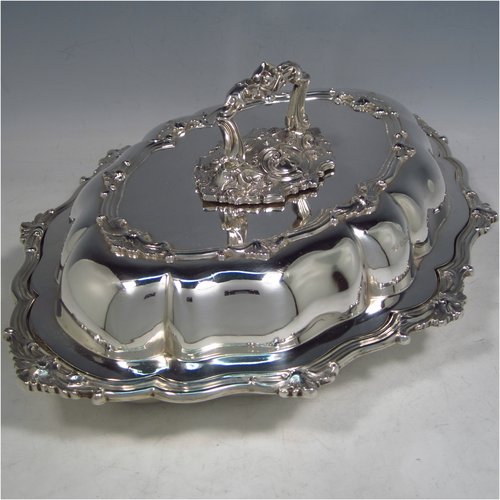 A very handsome Antique Sterling Silver pair of entree dishes, having oval lobed bodies, with lift-off lids, removable bayonet-fit handles, applied cast floral and scroll borders, and sitting on flat bases. These elegant silver entree dishes and covers were made by James Dixon & Sons of Sheffield in 1918. The dimensions of this fine pair of hand-made antique silver entree dishes and covers are length 35 cms (13.75 inches), width 26 cms (10.25 inches), and they weigh a total of approx. 3,472g (112 troy ounces).  