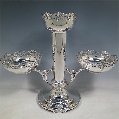 An Art Deco Sterling Silver table centrepiece or epergne, with hand-pierced geometrical style borders and Art Deco motifs, having one central flower vase, and two removable dishes resting on side arms, and all sitting on a pedestal base with four flanged feet. Made by James Dixon & Sons of Sheffield in 1934. The dimensions of this fine hand-made Art Deco style epergne or center-piece are height 33 cms (13 inches), width across arms 41 cms (16 inches), depth 16 cms (6.3 inches), and with a total weight of approx. 1,309 (42 troy ounces).   