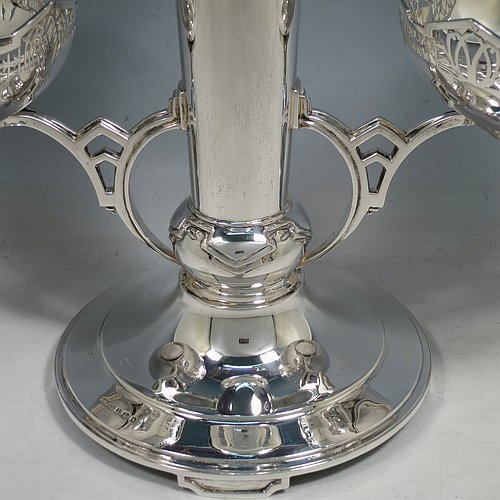 An Art Deco Sterling Silver table centrepiece or epergne, with hand-pierced geometrical style borders and Art Deco motifs, having one central flower vase, and two removable dishes resting on side arms, and all sitting on a pedestal base with four flanged feet. Made by James Dixon & Sons of Sheffield in 1934. The dimensions of this fine hand-made Art Deco style epergne or center-piece are height 33 cms (13 inches), width across arms 41 cms (16 inches), depth 16 cms (6.3 inches), and with a total weight of approx. 1,309 (42 troy ounces).   