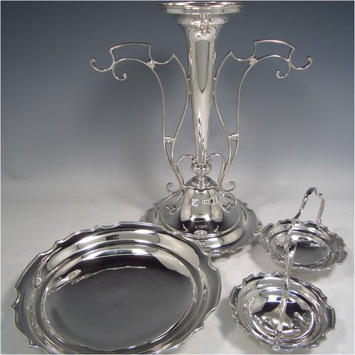 A Sterling Silver table Epergne centrepiece, having a removable central bowl, with two removable dishes on side arms, with applied scroll borders, an Art Nouveau style frame, and sitting on a spreading round base with four cushion feet. Made by the Deakin Brothers of Sheffield in 1924. The dimensions of this fine hand-made silver Epergne table centrepiece are height 32.5 cms (12.75 inches), width across arms 32 cms (12.5 inches), and it weighs a total of approx. 1,166g (37.6 troy ounces)   