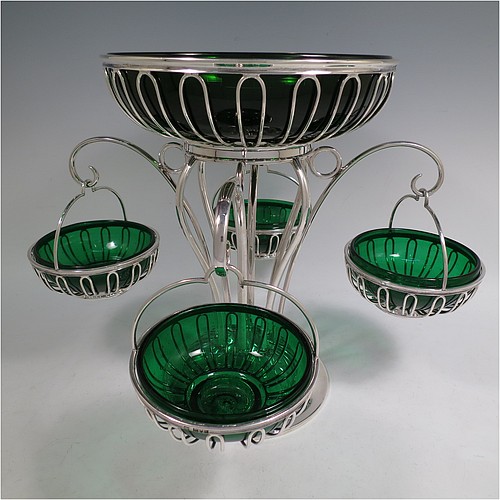 A very handsome and unusual Antique Edwardian Sterling Silver table Epergne centrepiece in an Art Nouveau style, having a removable central round wire-work basket and four matching removable swing baskets on side arms, all with dark green glass liners, and sitting on a spreading round base. Made by William Hutton of London in 1910. The dimensions of this fine hand-made antique silver Epergne table centrepiece are height 29 cms (11.5 inches), width across arms 38 cms (15 inches), and it weighs a total of approx. 1,954g (63 troy ounces)    