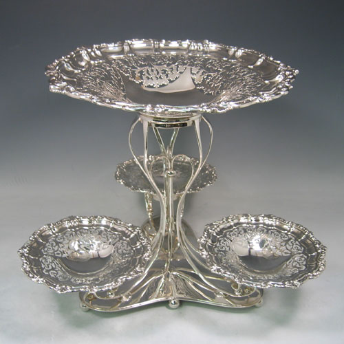 Sterling silver hand-pierced epergne, having four removable dishes, with one larger central dish, and three smaller dishes, all hand-pierced with applied shell and floral borders, sat in a wire-work frame on a spreading base with six ball feet. Made by Charles Widmer & Sons of Birmingham in 1912. Height 31 cms (12.25 inches), width 39.5 cms (15.5 inches). Total weight approx. 1,997g (64.4 troy ounces).