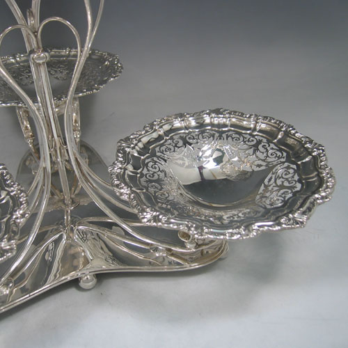 Sterling silver hand-pierced epergne, having four removable dishes, with one larger central dish, and three smaller dishes, all hand-pierced with applied shell and floral borders, sat in a wire-work frame on a spreading base with six ball feet. Made by Charles Widmer & Sons of Birmingham in 1912. Height 31 cms (12.25 inches), width 39.5 cms (15.5 inches). Total weight approx. 1,997g (64.4 troy ounces).