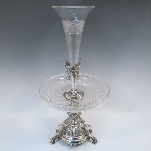 A very pretty Antique Victorian Sterling Silver table Epergne centrepiece, having a central cut crystal flower vase mounted above a matching round fruit bowl, all sitting on a lower silver body with hand-chased floral decoration, and three cast foliate feet. This beautiful silver and crystal epergne was made by Steven Smiley of London in 1876. The dimensions of this fine hand-made antique silver and crystal Epergne table centerpiece are height 53 cms (21 inches), and diameter of bowl 27 cms (10.5 inches),   