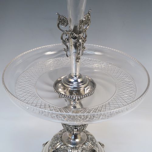 A very pretty Antique Victorian Sterling Silver table Epergne centrepiece, having a central cut crystal flower vase mounted above a matching round fruit bowl, all sitting on a lower silver body with hand-chased floral decoration, and three cast foliate feet. This beautiful silver and crystal epergne was made by Steven Smiley of London in 1876. The dimensions of this fine hand-made antique silver and crystal Epergne table centerpiece are height 53 cms (21 inches), and diameter of bowl 27 cms (10.5 inches),   