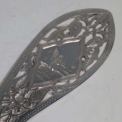 An Antique Victorian sterling silver and ivory-handled fish server slice, having a hand-cut ivory handle with leaf decoration, a hand-pierced symmetrical blade with floral decoration and an engraved scene of a fisherman on one side, together with a silver ferrule between the blade and handle. Made by George Unite of Birmingham in 1872. The length of this fine hand-made antique silver fish serving slice is 31 cms (12.25 inches).