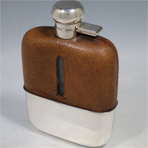 A large Sterling Silver and glass whisky flask, with leather skin mount, and a sight level both sides, having a bayonet fit lid and a pull-off cup with gold-gilt interior. Made by William Hutton & Sons of Sheffield in 1927. The dimensions of this fine hand-made silver and glass whisky flask are length 17 cms (6.75 inches), width 11.5 cms (4.5 inches), and depth 4 cms (1.5 inches).    