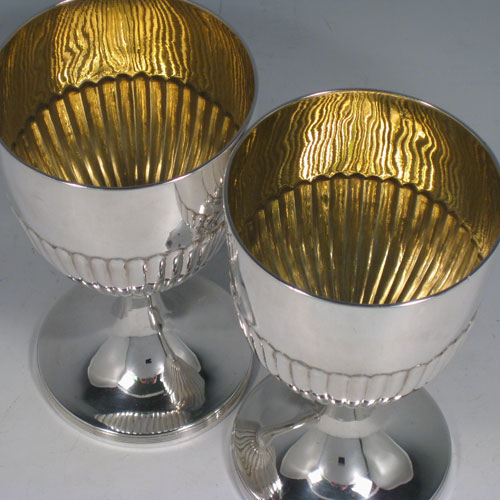 Antique Georgian sterling silver pair of goblets, having round bodies with hand-chased half-fluted decoration, gold-gilt interiors, and sitting on pedestal feet with reeded borders. Made by John Robins of London in 1803. The dimensions of this fine hand-made pair of silver goblets are height 16 cms (6.3 inches), diameter at top 9 cms (3.5 inches), and the total weight is approx. 517g (16.7 troy ounces).   