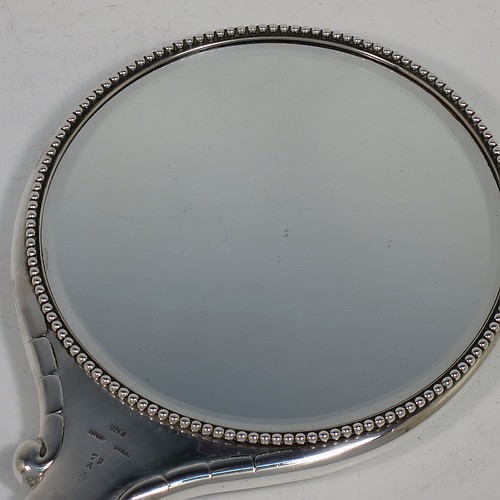 A very pretty and rare Arts and Crafts style Sterling Silver hand-mirror, having a round body with hand-hammered decoration and a hand-chased fluted border, the original bevelled mirror with an applied beaded border, and a central floral motif on the reverse. Designed and made by the famous Danish silversmith Georg Jensen,ca.1920. The dimensions of this fine hand-made Arts and Crafts style silver hand mirror are length 28.5 cms (11.25 inches), and diameter 14.5 cms (5.75 inches).    