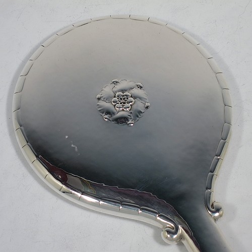 A very pretty and rare Arts and Crafts style Sterling Silver hand-mirror, having a round body with hand-hammered decoration and a hand-chased fluted border, the original bevelled mirror with an applied beaded border, and a central floral motif on the reverse. Designed and made by the famous Danish silversmith Georg Jensen,ca.1920. The dimensions of this fine hand-made Arts and Crafts style silver hand mirror are length 28.5 cms (11.25 inches), and diameter 14.5 cms (5.75 inches).    