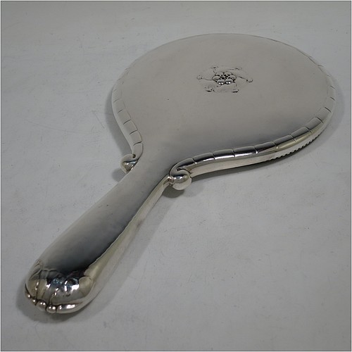 A very pretty and rare Arts and Crafts style Sterling Silver hand-mirror, having a round body with hand-hammered decoration and a hand-chased fluted border, the original bevelled mirror with an applied beaded border, and a central floral motif on the reverse. Designed and made by the famous Danish silversmith Georg Jensen,ca.1920. The dimensions of this fine hand-made Arts and Crafts style silver hand mirror are length 28.5 cms (11.25 inches), and diameter 14.5 cms (5.75 inches).    