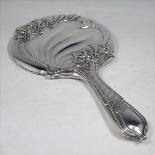 An Antique Edwardian Art Nouveau Sterling Silver hand-mirror, having a round body with hand-chased floral lilly decoration, and an original round bevelled mirror with rope-twist border. Made by Henry Williamson Ltd., of Birmingham in 1905. The dimensions of this fine hand-made antique silver hand mirror are length 28 cms (11 inches), and diameter 15 cms (6 inches). Please note that the mirror glass has very slight scratches concurrent with its age.   