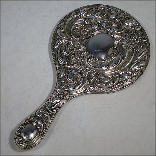 An Antique Edwardian Sterling Silver hand-mirror, having a round body with hand-chased floral decoration, a central vacant cartouche on the main body and an oval cartouche on the handle, and a round mirror. Made by William Neale of Chester in 1906. The dimensions of this fine hand-made antique silver hand mirror are length 28 cms (11 inches), and diameter 15 cms (6 inches).   