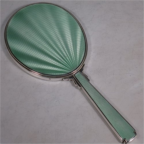 A Sterling Silver Art Deco style hand-mirror, having an oval body and a square cross-section handle, with green enamelled sun-burst style decoration, and an original bevelled mirror. Made by Robert Comyns of London in 1945. The dimensions of this fine hand-made Art Deco silver and green enamelled hand mirror are length 25.5 cms (10 inches), and width 11 cms (4.3 inches).    