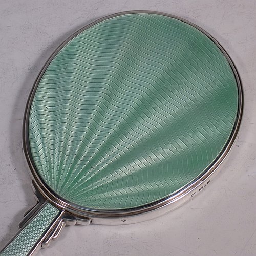 A Sterling Silver Art Deco style hand-mirror, having an oval body and a square cross-section handle, with green enamelled sun-burst style decoration, and an original bevelled mirror. Made by Robert Comyns of London in 1945. The dimensions of this fine hand-made Art Deco silver and green enamelled hand mirror are length 25.5 cms (10 inches), and width 11 cms (4.3 inches).    