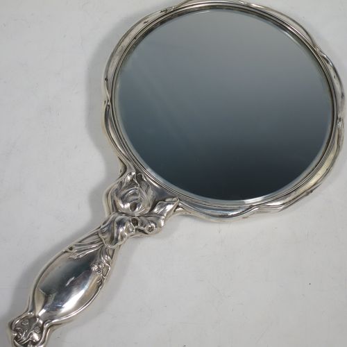 A very pretty Art Nouveau Antique Edwardian Sterling Silver hand-mirror, having a round body with hand-chased Iris floral decoration, and a round bevelled mirror with a lobed border. Made by William Aitken of Birmingham in 1909. The dimensions of this fine hand-made antique Art Nouveau silver hand mirror are length 28 cms (11 inches), and diameter 16 cms (6.25 inches).    